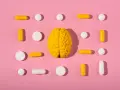 Żółty model mózgu otoczony białymi i żółtymi tabletkami i kapsułkami, symbolizującymi równowagę neuroprzekaźników, jak serotonina.