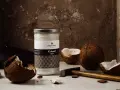 Ein Glas Kokosöl nativ steht neben zerbrochenen Kokosnüssen und einem Hammer. So wird aus der Frucht das wertvolle Öl gewonnen.