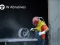 Pracownik w kasku i ochronnym ubraniu wykonuje piaskowanie aluminium felgi.