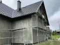 Dom w trakcie prac elewacyjnych. Widać rusztowania i szarą ścianę, która czeka na tynk silikonowy. Cena za m2 robocizny jest kluczowa dla budżetu.