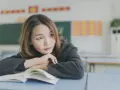 Młoda uczennica w szkole w Japonii, zamyślona nad otwartą książką.