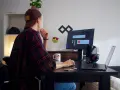 Młody mężczyzna w czapce i flanelowej koszuli pracuje przy komputerze. To typowy freelancer, który tworzy swoje projekty z domu.