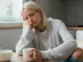 Zmęczona kobieta z blond włosami opiera głowę na dłoni, trzymając kubek. Może to być jeden z objawów keto grypy.