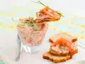 Rillettes de saumon crémeuses dans un verre, garnies de fines herbes et servies sur des toasts avec des tranches de saumon fumé.