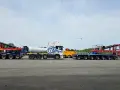 Ciężarówka z naczepą tandem przewozi element turbiny wiatrowej. Obok stoi inna naczepa z dźwigiem.