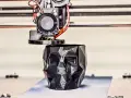 A 3D printer nozzle extrudes filament to create a faceted black skull planter, showcasing innovative 3D printing examples.