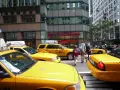 Żółte taksówki na ulicy Nowego Jorku. Rodzina z dzieckiem idzie ulicą, a obok nich stoi licencja taxi bez działalności.