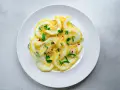 Dünne Scheiben Zitrone mit Zucker bestreut, garniert mit frischen Kräutern und Chiliflocken. Ein erfrischender Genuss!