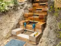Construction d'un escalier traverse bois et gravier. Des poutres de bois sont empilées pour former des marches dans une tranchée.