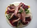 Lonchas de cerdo tierno sobre una cama de puré cremoso y pimiento del piquillo asado, decorado con perejil fresco.