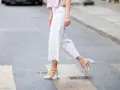 Mujer cruza la calle con un look comunión: pantalón blanco de corte ancho y sandalias de tiras.