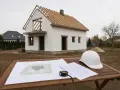 Na stole leżą plany i biały kask, obok budowa domu. Czy to będą domy bez pozwolenia, czy legalna inwestycja?