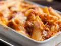 Un invitante piatto di pasta al forno, con penne ricoperte da un ricco sugo e formaggio filante, pronto per essere gustato.