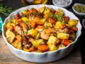 Pieczone podudzia z kurczaka z ziemniakami i marchewką, doprawione ziołami, w białej ceramicznej misie.