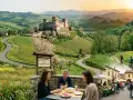 Scenic Italian countryside with a castle, vineyards, and people enjoying food and cycling, perfect for day trips from Parma, Italy.