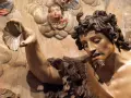 Detalle de escultura barroca: figura masculina con barba y cabello rizado sostiene una concha. Ángeles infantiles observan. Maestría de escultores del barroco.