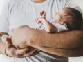 Tata tuli maleństwo, które nie chce spać. Dziecko wtula się w jego ramię, a na ramieniu taty widnieje tatuaż strzały.
