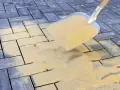 Schaufel mit Sand zum Terrassenplatten verfugen. Sand rieselt auf graue Pflastersteine.