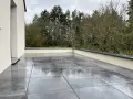 Terrasse avec dalles grises sur un toit plat, offrant une vue sur une forêt. L'étanchéité du toit plat est assurée pour une durabilité optimale.