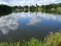 Spokojne jezioro na Kaszubach, odbijające chmury. W oddali widać łódkę i kościół. Idealne miejsce na wakacje.