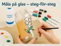 En hand målar en blomma på ett glas med en pensel. Material som isopropanol och färgpennor ligger bredvid.