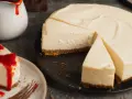 Ein cremiger New York Cheesecake, das Original-Rezept, mit einem Stück auf einem Teller, beträufelt mit roter Soße.