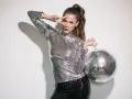 Kobieta w cekinowym topie i spodniach, z kulą dyskotekową w ręku, pozuje w stylu disco.