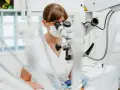 Dentystka pod mikroskopem precyzyjnie zakłada plombę. Dowiedz się, ile kosztuje plomba u dentysty.