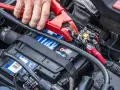 Starthilfe war zuerst: Eine Hand befestigt eine rote Klemme an der Autobatterie, um dem Fahrzeug wieder Leben einzuhauchen.