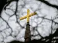 Goldenes Kreuz auf Kirchturmspitze, umrahmt von Ästen. Gedanken an die Kirchensteuer reduzieren.