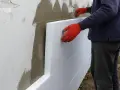 Pracownik w czerwonych rękawicach montuje styropian na ścianie. Zastanawiasz się, ile kosztuje ocieplenie domu 200m2?