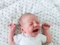 Płacz 6 tygodniowe dziecko na białej pościeli w kropki.