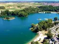 Der Mechtersheim See mit seiner türkisen Wasserfarbe, umgeben von grünen Bäumen und einem Campingplatz. Im Hintergrund erstrecken sich Felder und eine Stadt.