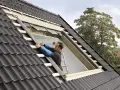 Budowa okienka w dachu. Pracownik montuje izolację i elementy konstrukcyjne, przygotowując miejsce na okno dachowe.