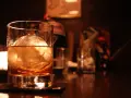 Ein Glas mit bernsteinfarbenem Whisky und einer großen Eiskugel steht auf einem dunklen Holztisch. Man trinkt Whisky mit Eis für den perfekten Genuss.