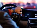 Kierowca w samochodzie ciężarowym do 3,5 tony sprawdza kilometrówkę na zegarku, jadąc nocą przez miasto.