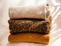 Gestapelte Strickwaren in warmen Herbstfarben. Damit die **Wolle bei 40 Grad waschen** gelingt, sind diese Pullover perfekt.