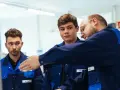 Drei junge Männer in blauen Arbeitskitteln lernen gemeinsam. Ein Ausbilder erklärt etwas, während die genz-Auszubildenden aufmerksam zuhören.