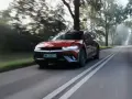 Czerwony Hyundai Ioniq 5 jedzie po wiejskiej drodze wśród drzew.