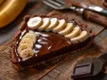 Une part de tarte banane chocolat, garnie de rondelles de banane fraîche sur une ganache onctueuse, sur un fond en bois rustique.