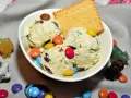 Schüssel mit cremigem Eis, garniert mit bunten Smarties und einem Keks. Kleine Figuren schmücken die Szene.