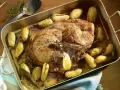 Rouelle de porc rôtie au four, entourée de pommes de terre dorées et d'herbes aromatiques. Un plat savoureux prêt à être dégusté.