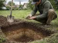 Mężczyzna w okopach analizuje próbki ziemi, wykonując badania geologiczne. Obok stoi łopata.
