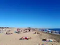Tłum ludzi odpoczywa na słonecznej plaży. Woda jest spokojna, a niebo bezchmurne. Czy Gran Canaria jest bezpieczna? Tak, wygląda na to, że turyści czują się tu swobodnie.