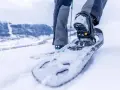 Piede con racchette da neve che affonda nella neve fresca, pronto per camminare in montagna.