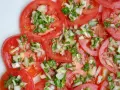 Fette di pomodoro fresco condite con cipolla tritata e erbe aromatiche. Un'insalata di pomodori semplice e gustosa.