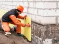Budowlaniec układa izolację na nierównych fundamentach. Jak zaizolować stare nierówne fundamenty? To klucz do ochrony domu.