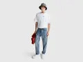 Uomo con t-shirt bianca "LOVE", cappello bucket grigio e jeans relaxed fit. Il significato di questi jeans è comfort e stile casual.