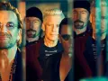 Le groupe U2, avec Bono au premier plan, pose en groupe, leurs visages reflétant une lumière tamisée.