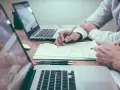 Deux personnes travaillent sur des documents et des ordinateurs portables, discutant du droit de la mode.